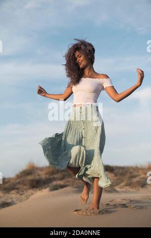 Von unten charmant glücklich weiblich im Sommer Outfit zu Fuß entlang Sandy Hill auf Hintergrund der Sonnenuntergang weg schauen Stockfoto