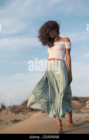 Von unten charmant glücklich weiblich im Sommer Outfit zu Fuß entlang Sandy Hill auf Hintergrund der Sonnenuntergang Blick nach unten Stockfoto