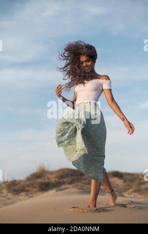 Von unten charmant glücklich weiblich im Sommer Outfit zu Fuß entlang Sandy Hill auf Hintergrund der Sonnenuntergang weg schauen Stockfoto