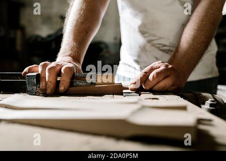 Crop männlichen Holzarbeiter stehen an alten Werkbank und arbeiten mit Holzdetails in grungy Werkstatt Stockfoto