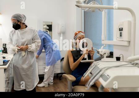 Weibliche Patientin sitzt auf dem Stuhl und schaut nach dem Spiegel Erhalten zahnärztliche Behandlung von professionellen Zahnärzten in der modernen Klinik Stockfoto