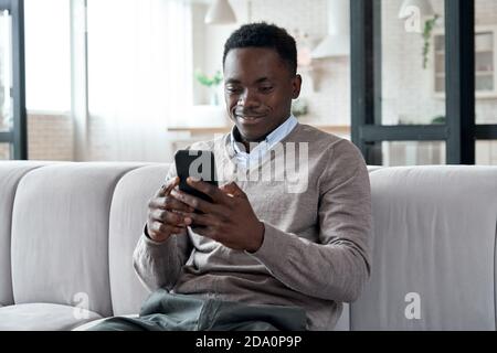 afroamerikanischer Mann mit mobilen Apps sitzen auf Couch zu Hause. Stockfoto