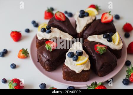 Nahaufnahme köstliche hausgemachte Schokoladenkuchen mit weißen und Schokoladencreme Mit frischen Beeren und Zitronenscheiben dekoriert und in Scheiben geschnitten Teile Stockfoto