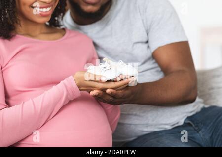 Von erwarteten afroamerikanischen Eltern, die kleine Babyschuhe halten, abgeschnitten Stockfoto