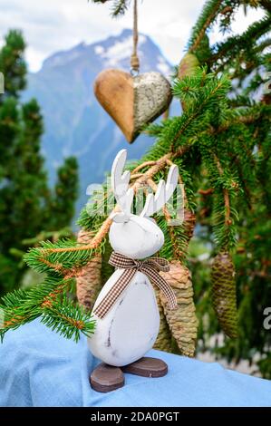 Grüner Weihnachtsbaum mit Zapfen, der in den französischen Alpen wächst Dekoriert mit hängendem Holzherz und weihnachtselch und Berg Peaks auf Backgr Stockfoto