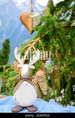 Grüner Weihnachtsbaum mit Zapfen, der in den französischen Alpen wächst Dekoriert mit hängendem Holzherz und weihnachtselch und Berg Peaks auf Backgr Stockfoto