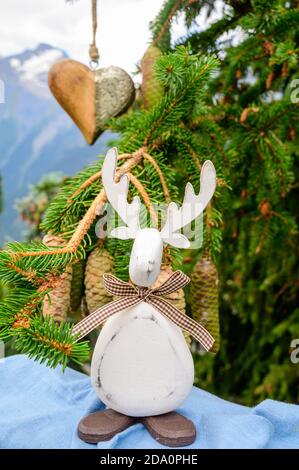 Grüner Weihnachtsbaum mit Zapfen, der in den französischen Alpen wächst Dekoriert mit hängendem Holzherz und weihnachtselch und Berg Peaks auf Backgr Stockfoto