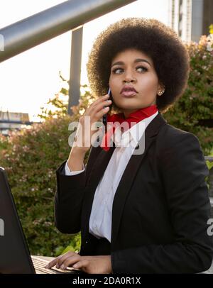 Seitenansicht des ernsten afroamerikanischen Unternehmers mit Telefonanruf Während der Arbeit auf Laptop sitzen auf Treppen Stockfoto