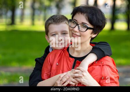 Porträt einer glücklichen Mutter, Teenager Sohn umarmt sie. Familienfreizeit in der Natur im Park, sonniger Herbsttag. Gesunde Beziehungen, Nähe. Stockfoto