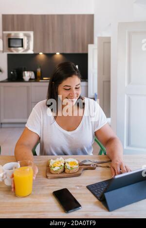 Lächelnde Frau, die zu Hause arbeitet und ein gesundes Frühstück hat Stockfoto
