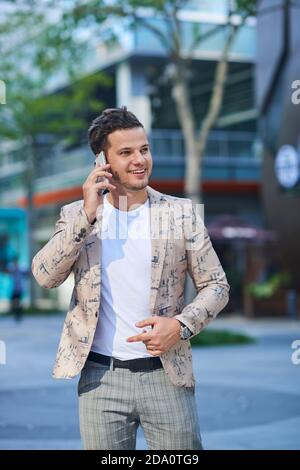 Junge fröhlich männlich in trendigen Kleidung reden auf Handy, während Blick in die Stadt Stockfoto