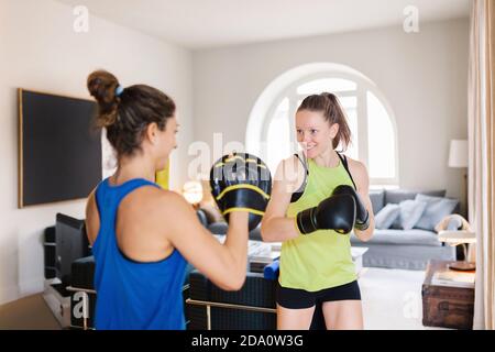 Passen weibliche Kämpferin in Handschuhe und persönliche Trainer im Boxen Fäustlinge stehen im Wohnzimmer und bereiten sich auf das Training vor Stockfoto