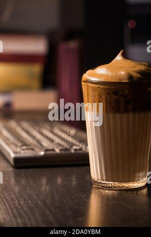 Ein Glas aromatischen kalten Dalgona Kaffee auf einem Holztisch serviert Im dunklen Zimmer Stockfoto