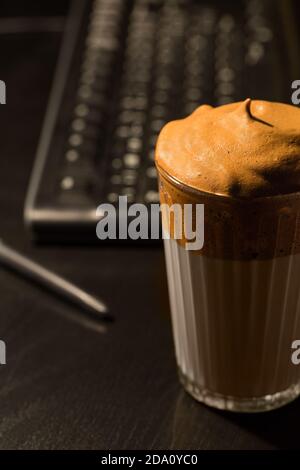 Ein Glas aromatischen kalten Dalgona Kaffee auf einem Holztisch serviert Im dunklen Zimmer Stockfoto
