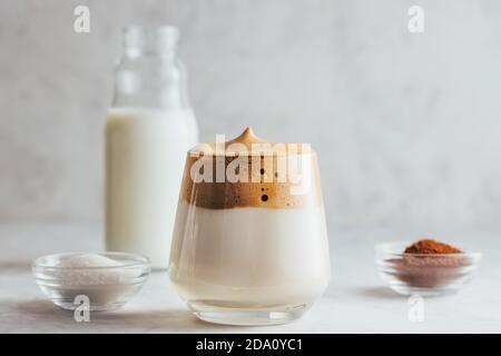 Aromatisches Dalgona-Getränk aus Glas auf Marmortisch mit einer Flasche Milch, Instant-Kaffee und Bohnen Stockfoto