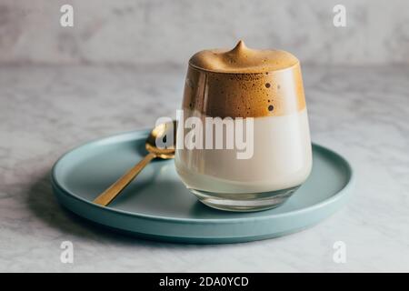 Schmackhafter kalter Dalgona Kaffee im Glas serviert auf blauem Teller Auf Betontisch Stockfoto