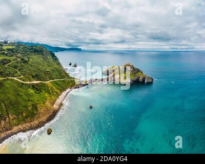 Drone Blick auf Pflastersteinweg entlang Steinbrücke Und Grat des felsigen Hügels zum einsamen Haus auf der Insel Gaztelugatxe umgeben von ruhigen Meer wa Stockfoto