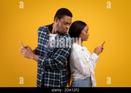 Strict Millennial african american guy Look, Frau in casual, SMS auf Smartphone und hat romantische Online-Beziehung Stockfoto