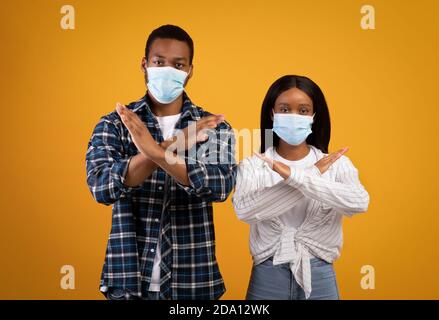 Serious Millennial african american Kerl und Dame in Schutzmasken kreuzen die Arme, Zeichen zeigend Stockfoto