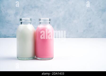Rosa und weiße Milchshakes in Flaschen auf weißem und grauem Hintergrund. Stockfoto