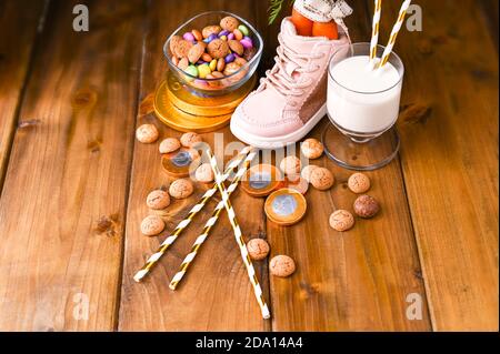 Traditionelle niederländische Urlaubspostkarte Sinterklaas. Holzhintergrund mit Kinderschuh mit Karotten für Santa's Pferd, Pepernoten und Süßigkeiten. Blick von oben. Speicherplatz kopieren. Hochwertige Fotos. Stockfoto