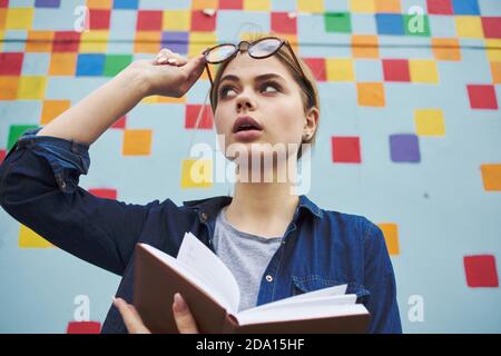 Ein Student in einem Hemd und einer Brille hält ein Buch In den Händen auf der Straße in der Nähe des Graffiti auf Die Wand Stockfoto