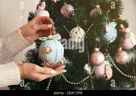 Nahaufnahme der weiblichen Hände hängen den Ball auf den Baum. Weihnachtsdekoration, Spielzeug am Baum hängen, Weihnachtsbaumkugel. Konzept für Neujahr und Weihnachtsferien Stockfoto