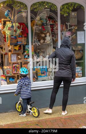 Eine junge Frau und ein kleines Kind, die auf einem Fahrrad fahren, schauen in einem Schaufenster auf Spielzeug an einem regnerischen Tag. Stockfoto