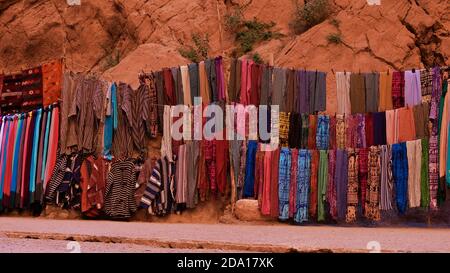 Bunte traditionelle Berber Kleidung und Teppiche zum Verkauf in der berühmten Todgha Schlucht in der Nähe von Tinghir, Marokko im südlichen Atlasgebirge angeboten. Stockfoto