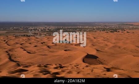 Schöner Panoramablick über die Sanddünen von Erg Chebbi mit Spuren im Sand und touristischen Dorf Merzouga, Süd-Marokko, Afrika an sonnigen Tag. Stockfoto