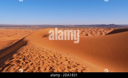 Schöner Panoramablick über die windförmigen Sanddünen von Erg Chebbi mit Spuren und Spuren im Sand in der Nähe von Merzouga, Süd-Marokko, Afrika. Stockfoto