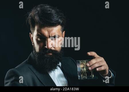 Fröhlicher bärtiger Mann trinkt teuren Whisky. Modischer Mann in weißem Hemd und Strapshaltern. Stockfoto