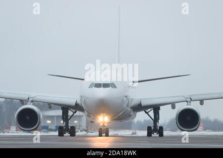 Nahaufnahme der Fahrgeschäfte mit dem Passagierflugzeug nach der Landung in der Dämmerung, Vorderansicht, Winterzeit. Inklusive Landescheinwerfer am Flugzeug. Luftfahrtindustrie Stockfoto
