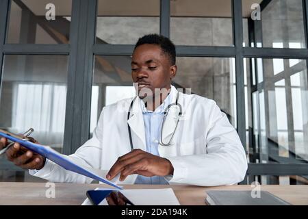 Schwarzer männlicher Arzt, der die Testergebnisse des Patienten mittels virtueller telemedizinischer Beratung überprüft. Stockfoto