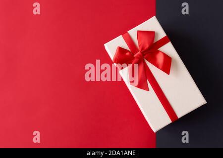 Weißes Geschenk mit rotem Band auf dem leuchtend roten Hintergrund Stockfoto