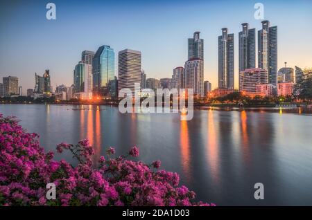 See mit violetten Blumen im City Park unter Wolkenkratzern bei Sonnenaufgang. Benjakiti Park in Bangkok, Thailand Stockfoto