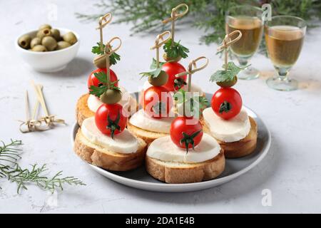 Kanapees von Mozzarella, Kirschtomaten, grüne Oliven, Petersilie auf Croutons von weißem Brot auf grauem Hintergrund. Festlicher Neujahrsnack. Nahaufnahme Stockfoto