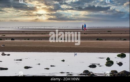 Paar, die bei Ebbe am Sandstrand spazieren gehen, mit farbenprächtiger Abenddämmerung am Himmel bei Sonnenuntergang, Firth of Forth, Schottland, Großbritannien Stockfoto