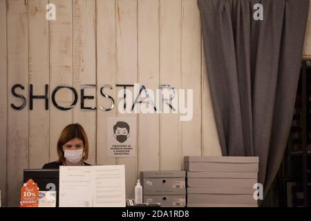 BELGRAD, SERBIEN - 4. OKTOBER 2020: Mitarbeiter eines Schuhwarenladens Schuhgeschäft neben einem Schild stehend, der bittet, eine Maske zu tragen, trägt eine Atemschutzmaske Stockfoto