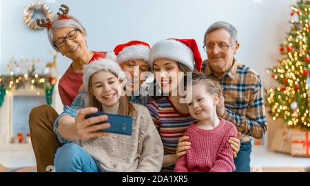 Frohe Weihnachten und schöne Feiertage! Oma, Opa, Mama, Papa und Kinder machen Selfie-Foto. Eltern und Töchter haben Spaß in der Nähe von Baum drinnen. L Stockfoto