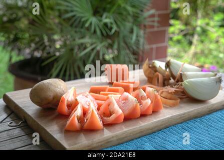 Tomaten, Karotten, Zwiebeln und Kartoffeln auf Holzschneidebrett schneiden. Vorbereitung auf eine gesunde Mahlzeit. Stockfoto