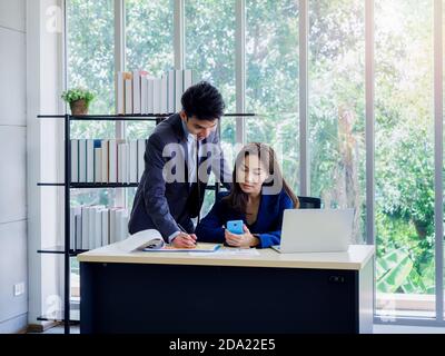 Asiatische Geschäftsfrau und Geschäftsmann tragen Anzug arbeiten zusammen im Büro. Junge männliche Angestellte stehen und beraten Jobs mit weiblichen Chef, während sie Stockfoto