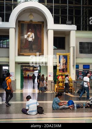 Die Eingangshalle am Bahnhof Hua Lamphong in Bangkok, mit Leuten, die auf dem Boden sitzen, warten. Das große Foto an der Wand zeigt König Chulalo Stockfoto