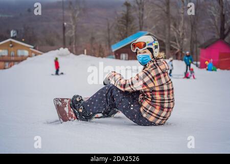 Frau Snowboarderin trägt eine medizinische Maske während COVID-19 Coronavirus auf Ein sonniger Wintertag in einem Skigebiet Stockfoto