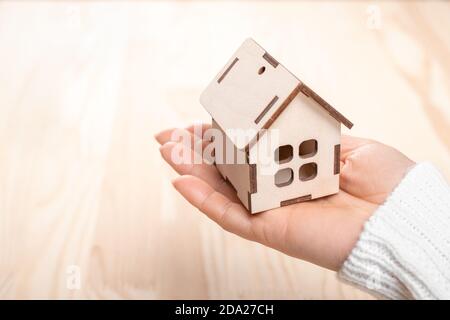 Kleines Holzhaus in der Hand einer Frau auf Holzhintergrund. Nahaufnahme eines kleinen Holzhauses in der Hand der Frau. Konzept des Kaufens neuer Wohnung. Stockfoto