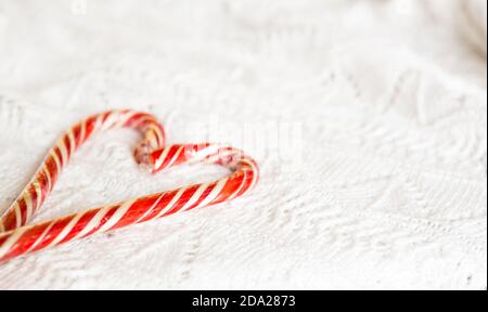 Weihnachts-Zuckerrohr gestreifter Weihnachtsmann in Herzform auf einer weißen Strickdecke. Ein Symbol der Liebe, ein Geschenk an einen geliebten Menschen, ein süßer Leckerbissen. Neujahr. Stockfoto
