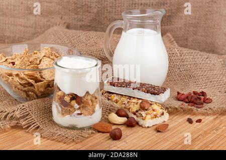 Gesundes Frühstück mit Joghurt, Milch, Müsliriegel, aber getrocknete Beeren auf rustikalem Hintergrund Stockfoto