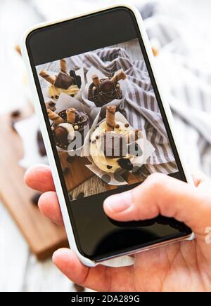 Mädchen macht ein Foto von Cupcakes auf einem Smartphone Stockfoto