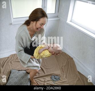 Glückliche Mutter hält das Baby und lacht beim Spielen auf dem hellen Balkon. Stockfoto