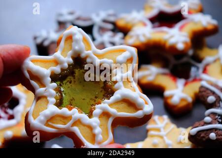 Finger halten Buntglaskekse mit grüner Mitte, mehr Cookies im Hintergrund Stockfoto